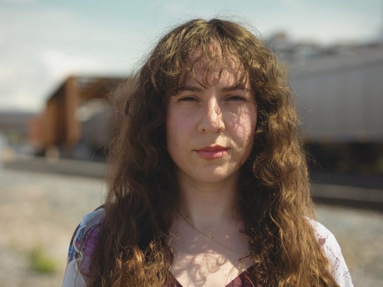 Woman looks straight at the camera. Long brown wavy hair.